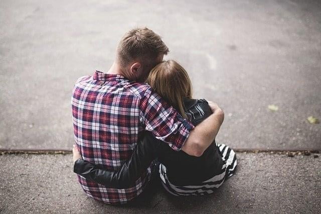 couple sitting on concrete driveway, hugging, looking at the distance