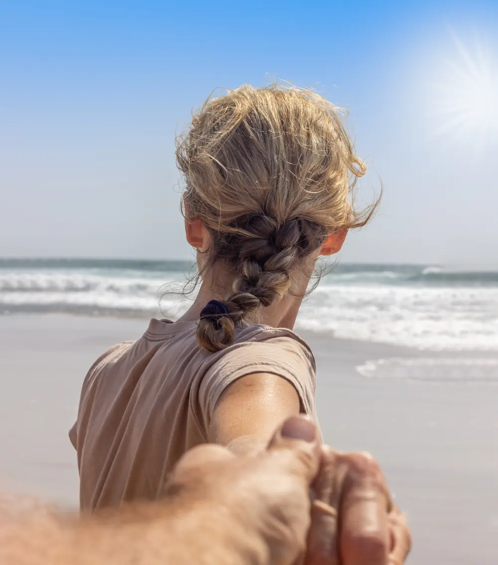 woman leading a man by the hand towards the ocean