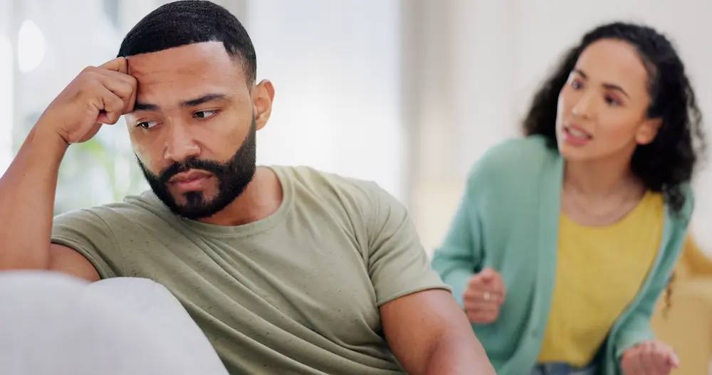 Man looking distressed while his partner speaks - Finding Peace Counseling Service PLLC - Finding Peace Counseling Service PLLC Man looking distressed while his partner speaks in the background, representing the emotional impact of infidelity on a relationship.